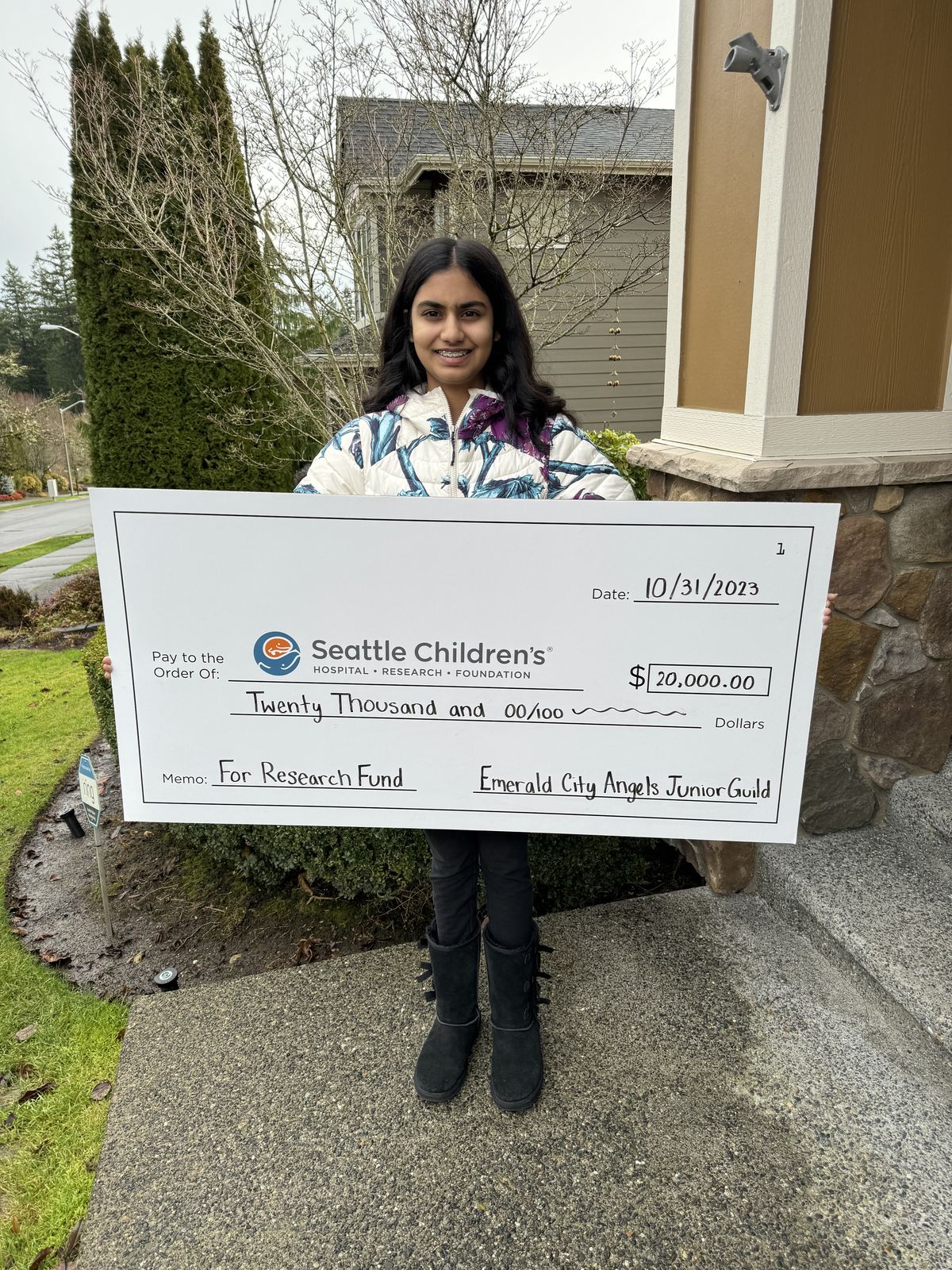 Monica holding an oversized check made out to Seattle Children’s for $20,000, dated October 31, 2023, with the memo line ‘For Research Fund’